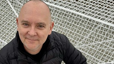 Man in black jacket smiles against white geometric mesh background.