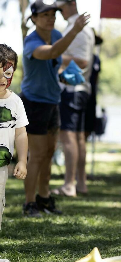 Families and children playing on the grassy lakeside lawn under shady trees