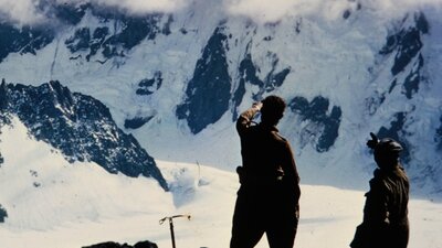 Two people in a snowy landscape pointing towards a mountain