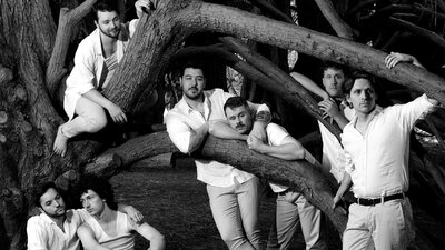 A group of people standing amonst the branches of a tree in white clothing, looking at the camera