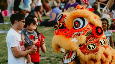 Image of a dragon dancer greeting a man and baby