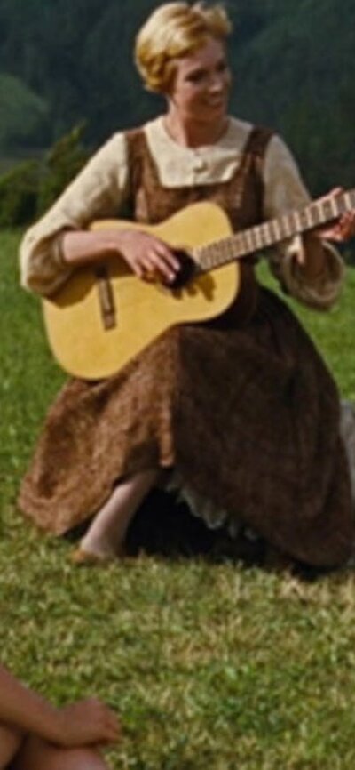 Woman in green field playing guitar to children sitting around her