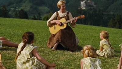 Woman in green field playing guitar to children sitting around her