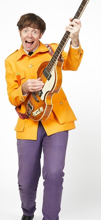 Sir Paul McCarrotney the Bassist wearing an orange suit and purple pants