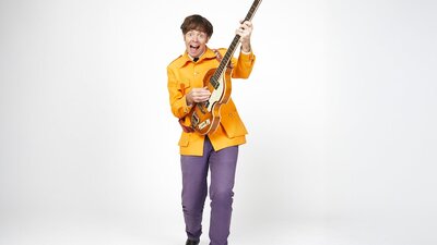 Sir Paul McCarrotney the Bassist wearing an orange suit and purple pants