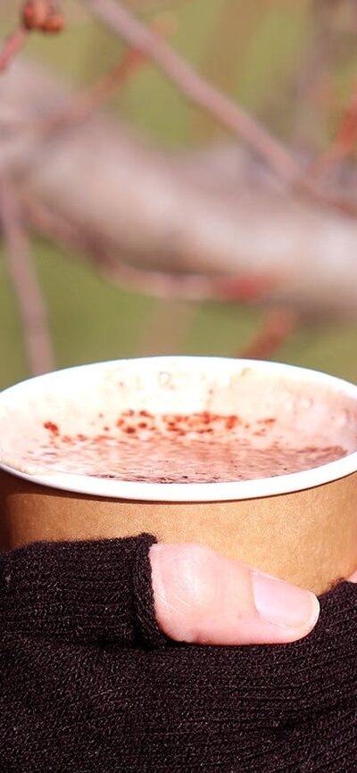 A pair of gloved hands clasp a disposable mug of hot chocolate