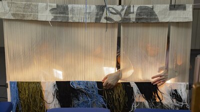 The back of a tapestry being woven by people on the other side