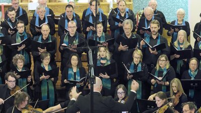 Choir singing, Anthony Smith playing piano, stringed instrument players, conducted by Dan Walker