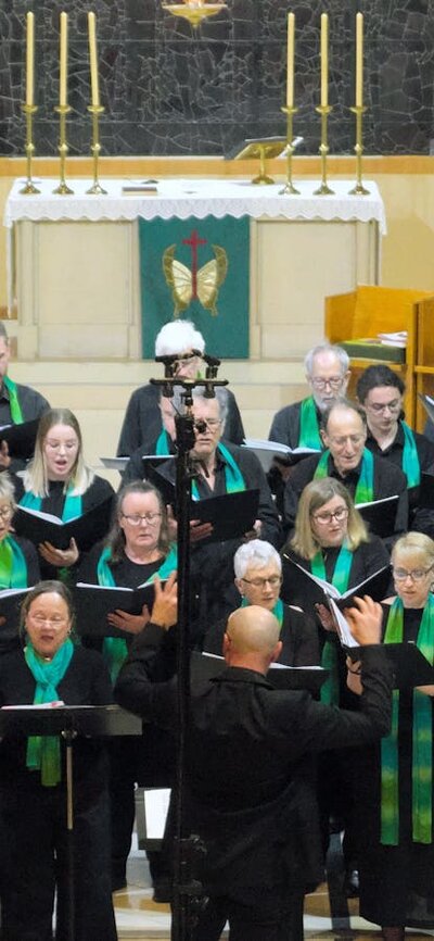 Choir singing on the altar steps, with Dan Walker conducting and Lindy Reksten, cello, at choir left