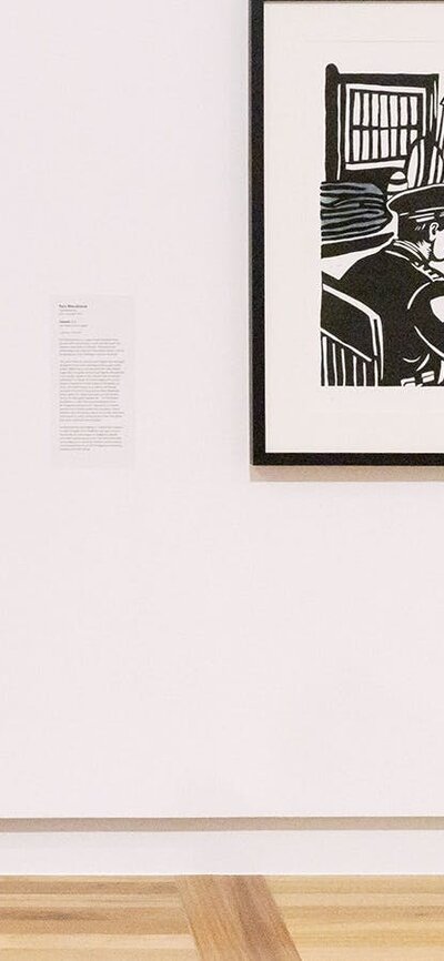 A person wearing a pink dress walks by a Gallery wall, looking at several artworks.