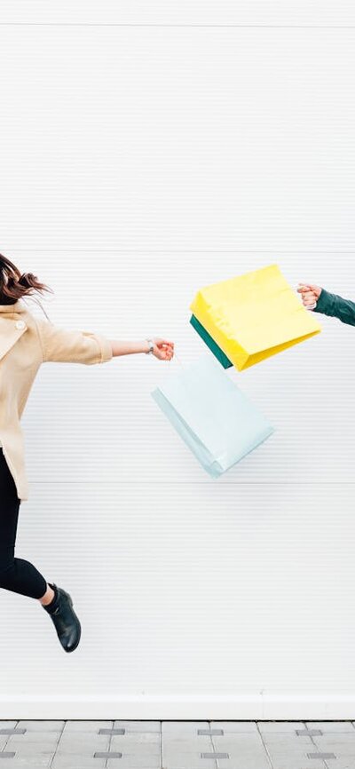 A man and a women holding shopping bags jumping in the air and smiling.