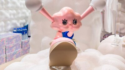 Pink cartoon character with large eyes and extended ears sits on fluffy white clouds