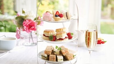 Array of sandwiches and treats on platters on a table with a white tablecloth and various decor.