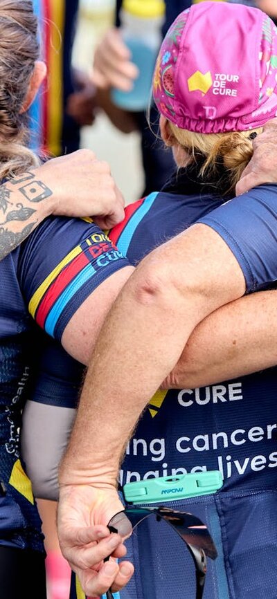 Signature Tour cyclists in kit, in a huddle with arms around each other,  taken from behind them