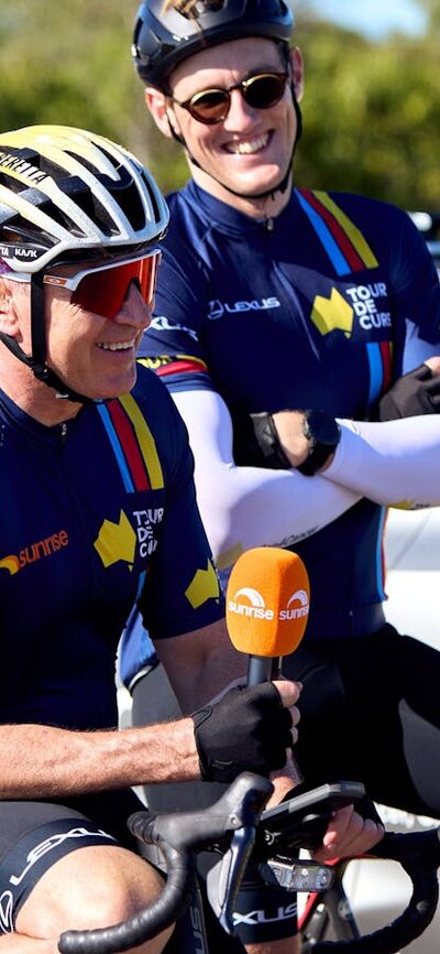 Mark Beretta and Mack Horton casually sitting on their bikes in cycle kit during Signature Tour '25