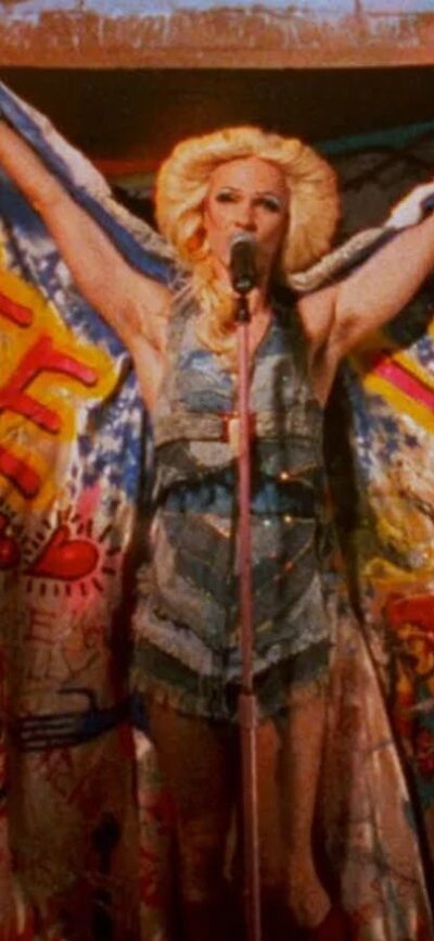 Person performing wearing wings, a wig and vibrant costume