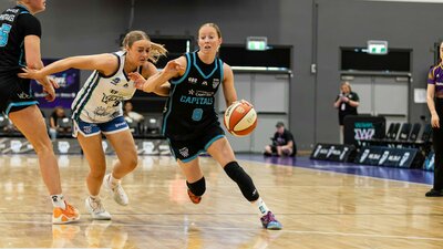 Women bounces basketball while being heavily defended.