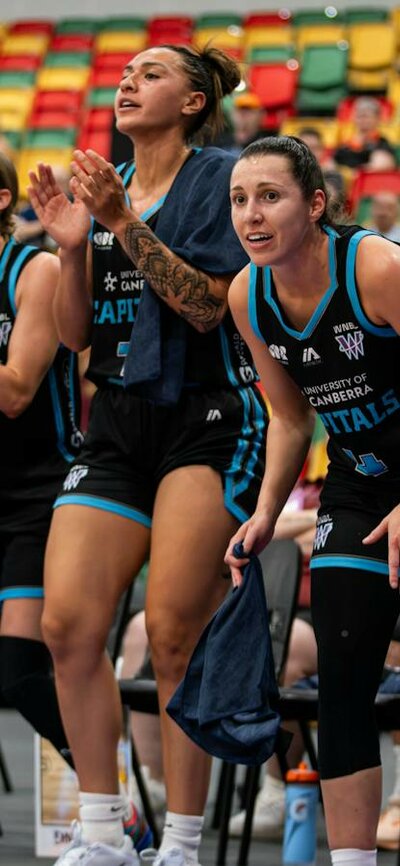 Four basketball players cheer while sitting on the side of the court.