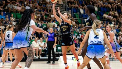 Female basketball player puts up a shot attempt surrounded by opponents.