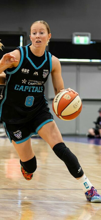 Women bounces basketball while being heavily defended.