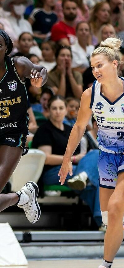 Basketball player runs down the court with defender in tow.