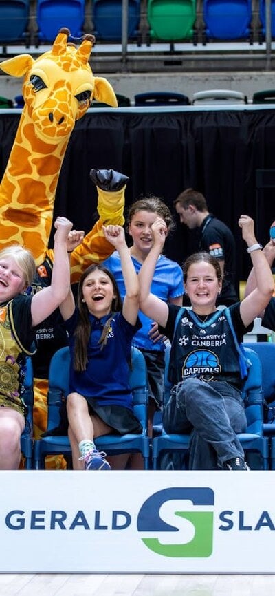 A group of young UC Capitals fans cheering while sitting courtside in a row.