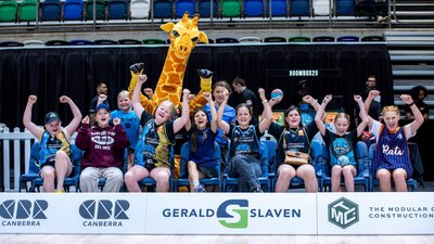 A group of young UC Capitals fans cheering while sitting courtside in a row.