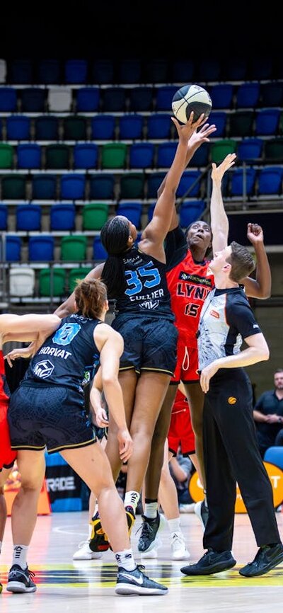 Basketball players mid-jump while competing for the tip-off.