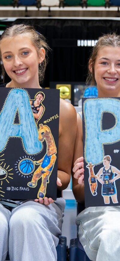 UC Capitals fans smiling while sitting courtside with posters of the athletes.
