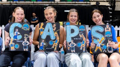 UC Capitals fans smiling while sitting courtside with posters of the athletes.