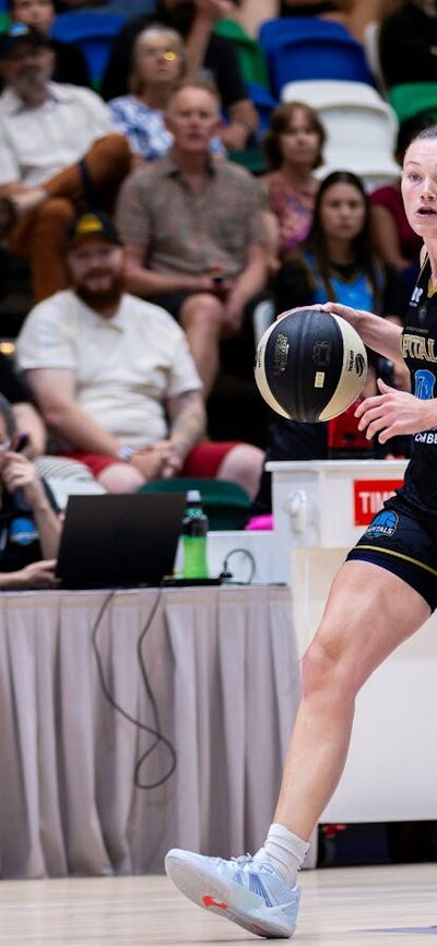 UC Capitals player dribbling a basketball while being defended.