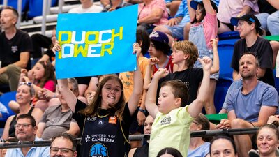Two young fans cheering in the stands while waving a UC Capitals poster.