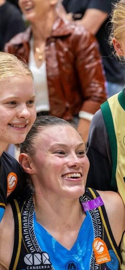 UC Capitals player smiling and posing for a photo with two young fans after a WNBL game.