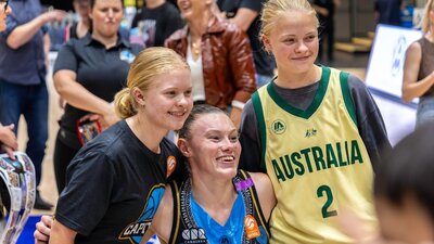 UC Capitals player smiling and posing for a photo with two young fans after a WNBL game.