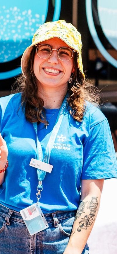 Happy UC staff member in blue shirt, holding a blue campus tours sign