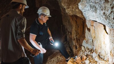 Two people using a torch to look at a large rock