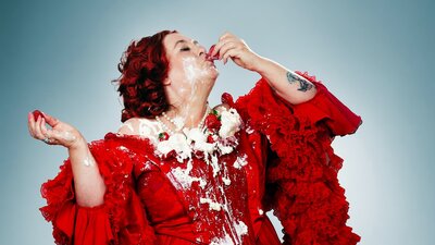 Nicky Barry is umladylike. Nicky Barry dressed in a 18th century red gown devouring strawberries and cream.
