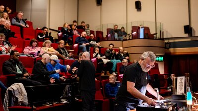 Vinyl Lounge Reconciliation Week 2025 Audience in a theatre and a man at the front preparing to play a vinyl
