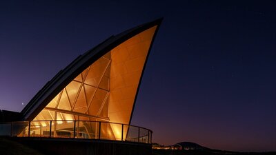 The triangular roof of the Margaret Whitlam Pavilion lights up against an evening sky