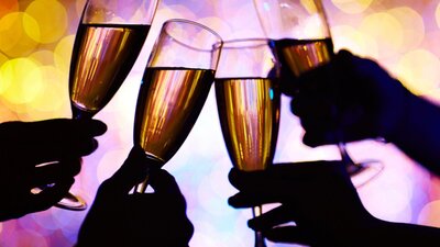 four wine glasses clinking with bright lights in background