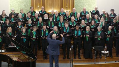 Choristers performing in front of altar, Dan Walker conducting, grand piano to his left.
