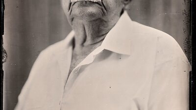 A black and white image of a man with a mustache and glasses with a stern look