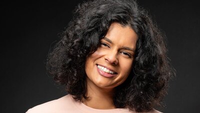 A woman smiling with curly hair in a pink shirt