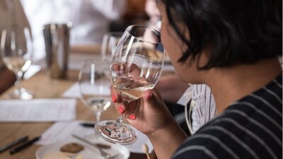 Learn how to taste wine with Canberra Cellar Door A young woman brings a glass of white wine to her nose.