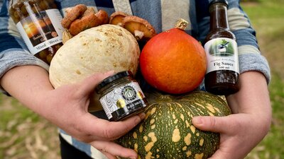 Local produce for the Winter Market Hands hold pumpkins, jars of olives and more.
