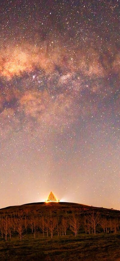 A purple night sky is scattered with stars. The dark landscape below is silhouette by glowing light