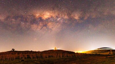 A purple night sky is scattered with stars. The dark landscape below is silhouette by glowing light