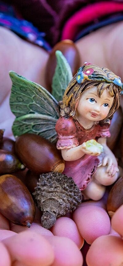 A child holds colourful seeds and a small purple fairy figurine