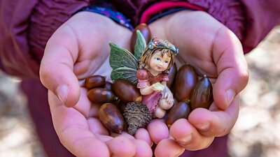 A child holds colourful seeds and a small purple fairy figurine