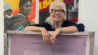 Alison Alder A woman with blonde hair and glasses leaning on a purple artwork piece.